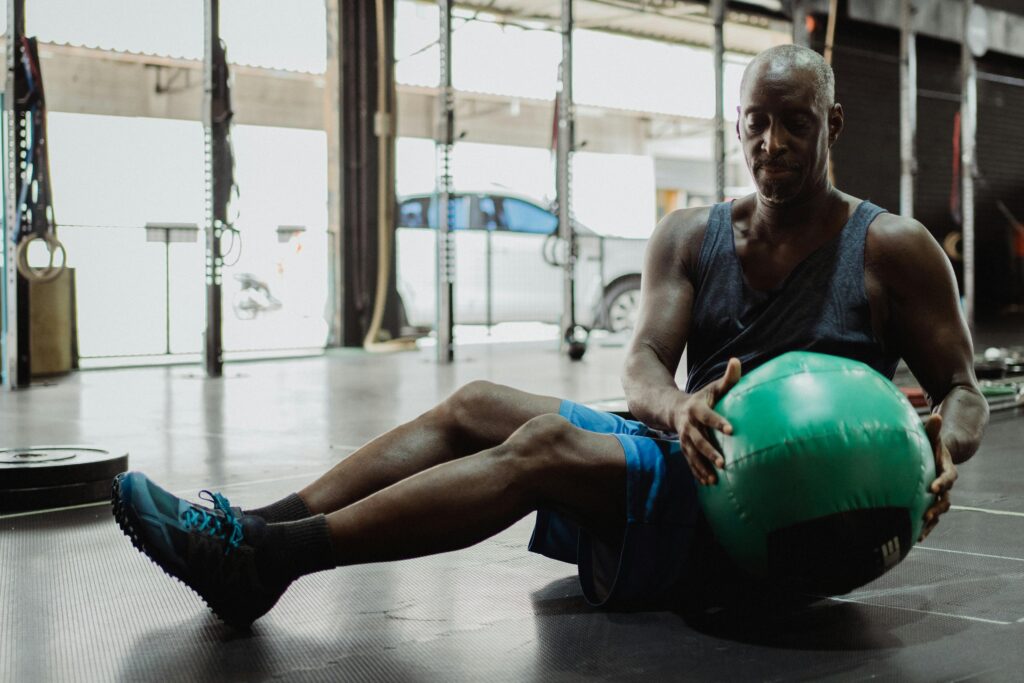Focused man doing an ab workout with a green exercise ball in a gym.